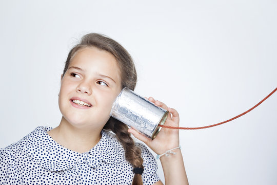 Happy smiling child using a can as telephone against gray backgr