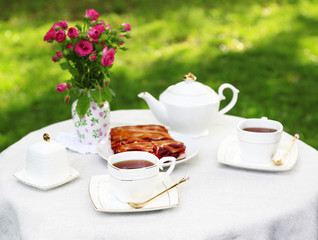 Coffee table with teacups and tasty pie in garden