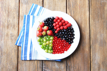 Forest berries on plate, on color wooden background