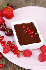 Ripe sweet berries and liquid chocolate on wooden table