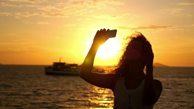 Girl Taking Picture with Smart Phone against Sunset and Sailing