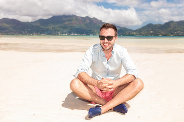 smiling young man with sunglasses sitting on a beach