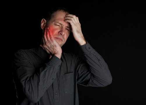 Man with a sick tooth keeps cheek hand. On a black background