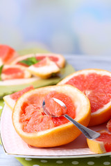 Ripe grapefruits on plate, on wooden table, on light background