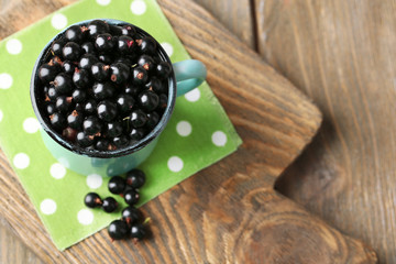 Ripe blackcurrants in mug on board, on wooden background.