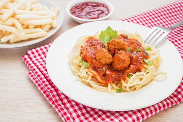 Spaghetti with meatballs in tomato sauce and french fries