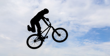 Silhouette of a man doing an jump with a bmx bike.