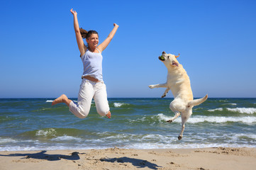 Woman and dog breed Labrador jumping on the beach - 67446753