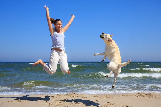 Woman And Dog Breed Labrador Jumping On The Beach