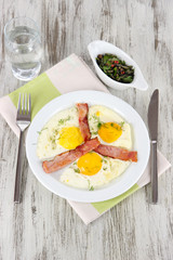 Scrambled eggs and bacon on plate on napkin on wooden table