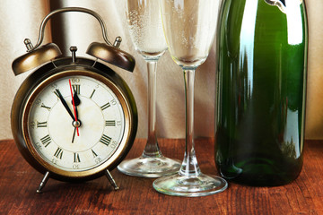 Alarm clock with champagne on table on golden cloth background