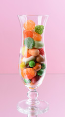 Different colorful fruit candy in glass on pink background