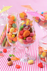 Different colorful fruit candy in glasses on pink background