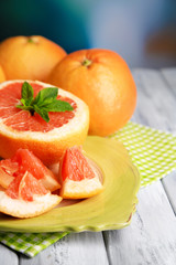 Ripe grapefruits on plate on color wooden background