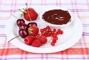 Ripe sweet berries and liquid chocolate on tablecloth