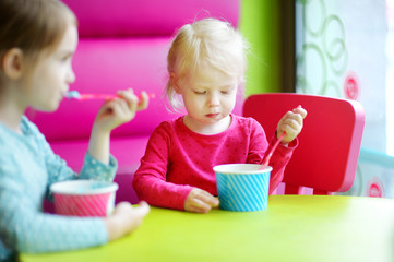 Two cute little sisters eating ice cream together