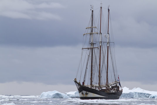 small sailing ship in Antarctic waters between ice floes and ice