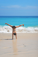 Девушка занимается акробатикой на пляже океана