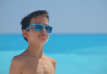 Fototapeta premium Portrait of young boy wearing sunglasses and posing by sea