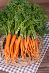 Bunch of fresh carrots with green leaves over wooden background