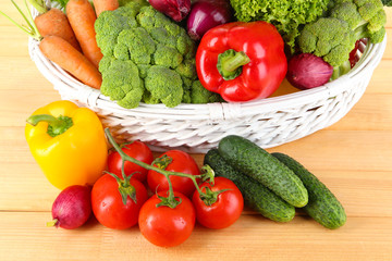 Fresh vegetables in white wicker basket on wooden background