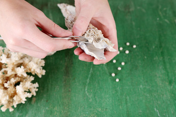 Hand with tweezers holding pearl and oyster on wooden