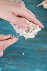 Hand with tweezers holding pearl and oyster on wooden