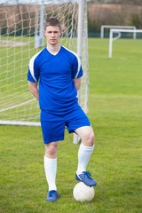 Football player in blue posing with the ball on pitch