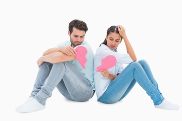 Sad couple sitting holding two halves of broken heart