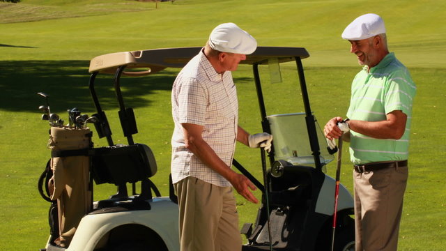 Two male friends chatting on the golf course by their kart