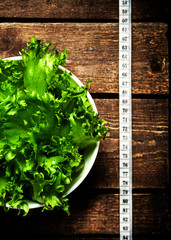 Fresh Fitness salad and measuring tape on rustic wooden table.