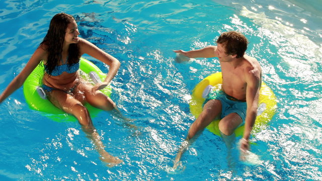 Couple sitting on inflatable rings in the swimming pool
