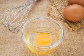 Fresh egg in bowl and metal whisk
