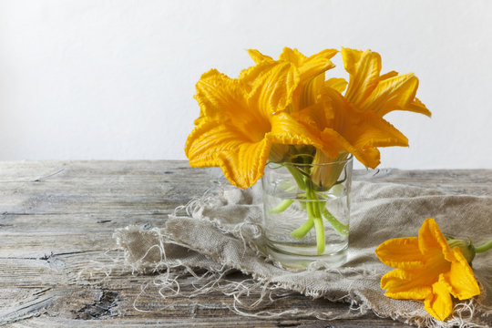 zucchini flowers on water glass on rustic table with napkin