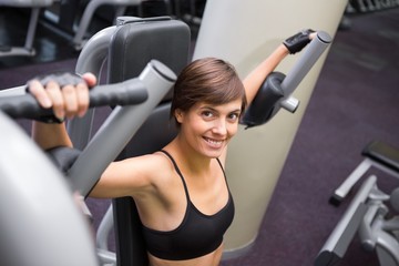 Fototapeta premium Smiling brunette using weights machine for arms