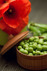 Green peas in bowl on wooden background with red poppy