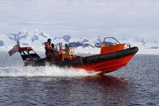 orange boat sailing at high speed in Antarctic waters against mo