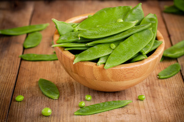 young green peas pods in a bowl on a wooden background