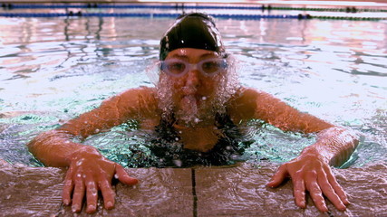 Fit swimmer emerging from pool and pulling herself up