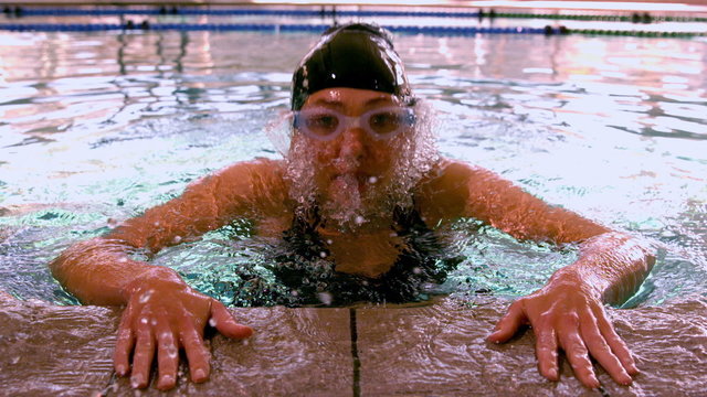 Fit swimmer emerging from pool and pulling herself up