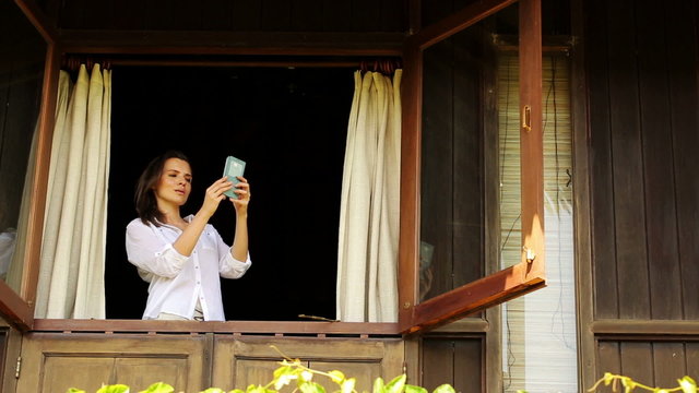 Woman taking photo with cellphone from window in country house