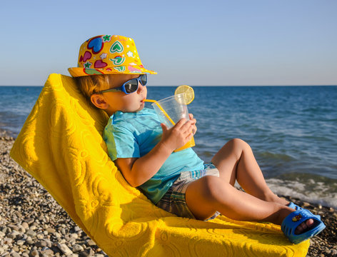 Boy kid in armchair with juice glass on beach