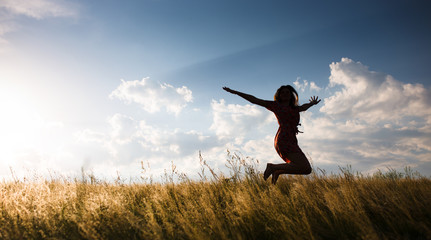 Happy woman jumping in the meadow at the sunset