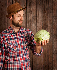 Happy farmer holding cabbage on rustic wood