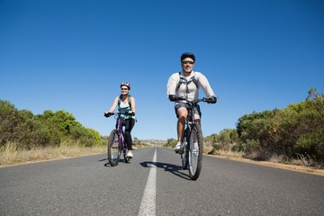 Fit smiling couple going for a bike ride in the countryside