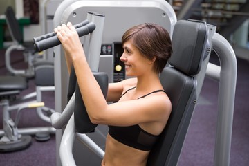 Fototapeta premium Happy brunette using weights machine for arms