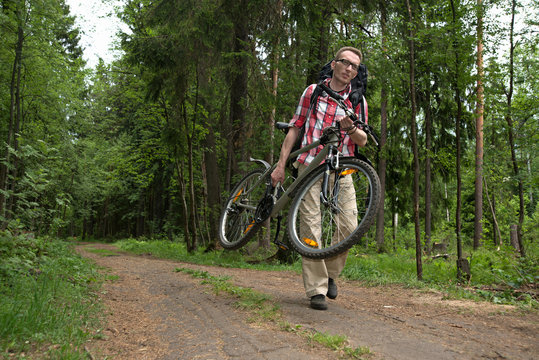 Tourist carrying his broken bike on the forest road