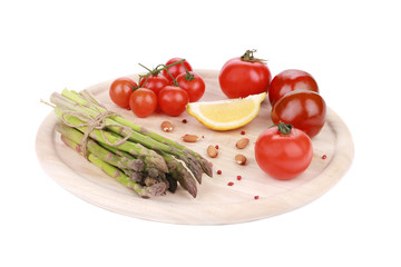 Asparagus and tomatoes on wooden board.
