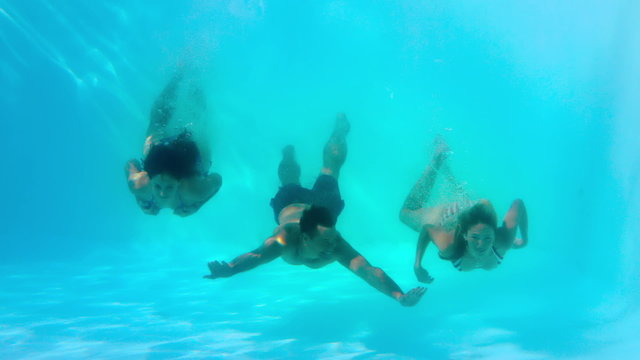 Friends swimming underwater in pool together