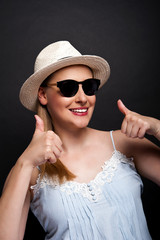 woman in hat and sunglasses showing ok thumbs over dark banckgro